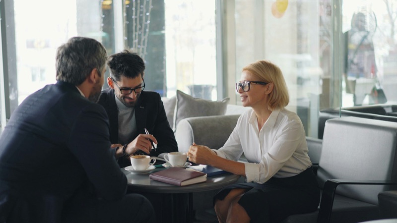 Drei Menschen im Gespräch an einem Café-Tisch.